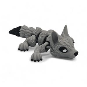 Peut inclure: Un jouet articul&eacute; en forme de renard gris avec une queue noire et des coussinets noirs. Le jouet est en plastique et pr&eacute;sente un design d&eacute;taill&eacute;, avec des articulations visibles et une surface textur&eacute;e. Le renard est couch&eacute;, sa t&ecirc;te et ses pattes sont visibles.