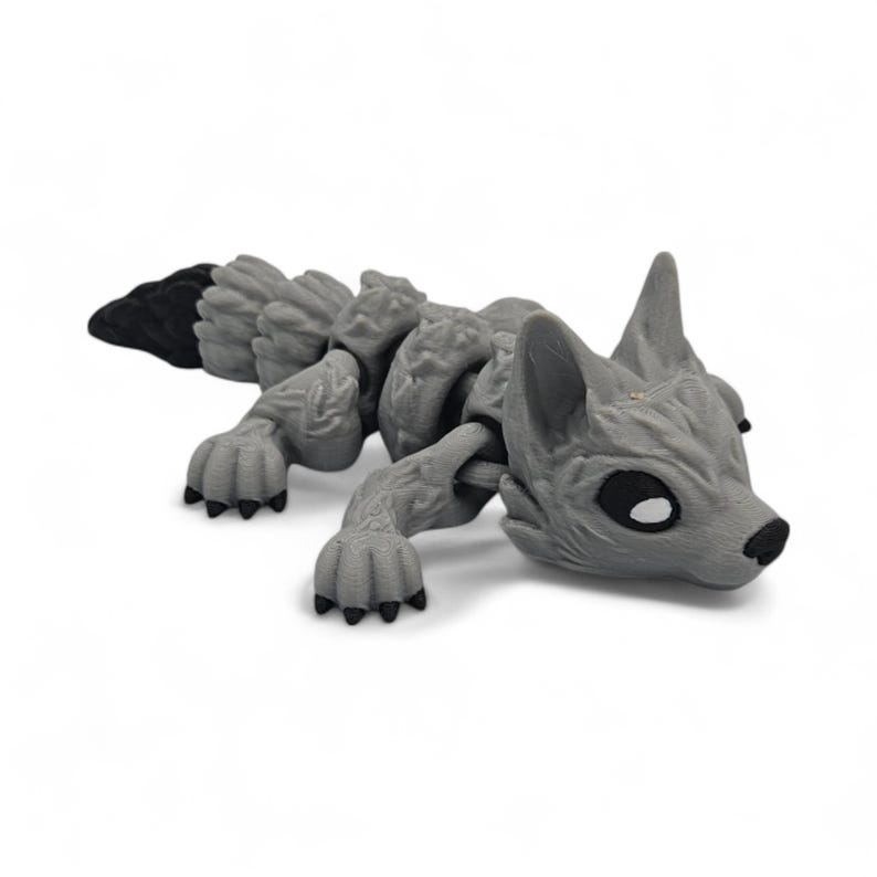 Peut inclure: Un jouet articul&eacute; en forme de renard gris avec une queue noire et des coussinets noirs. Le jouet est en plastique et pr&eacute;sente un design d&eacute;taill&eacute;, avec des articulations visibles et une surface textur&eacute;e. Le renard est couch&eacute;, sa t&ecirc;te et ses pattes sont visibles.
