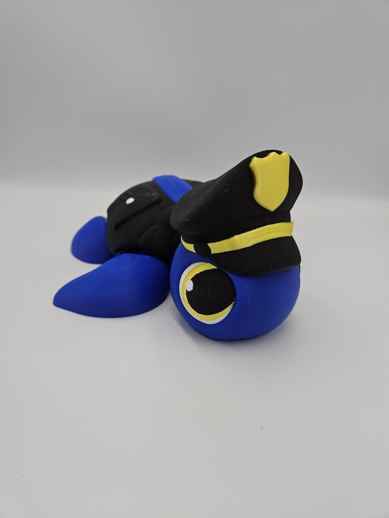 Pode incluir: Um personagem de desenho animado azul, preto e amarelo usando um chap&eacute;u de policial. O personagem tem um corpo azul grande e redondo, p&eacute;s azuis e uma parte traseira preta. O chap&eacute;u de policial &eacute; preto com uma faixa e um distintivo amarelos.
