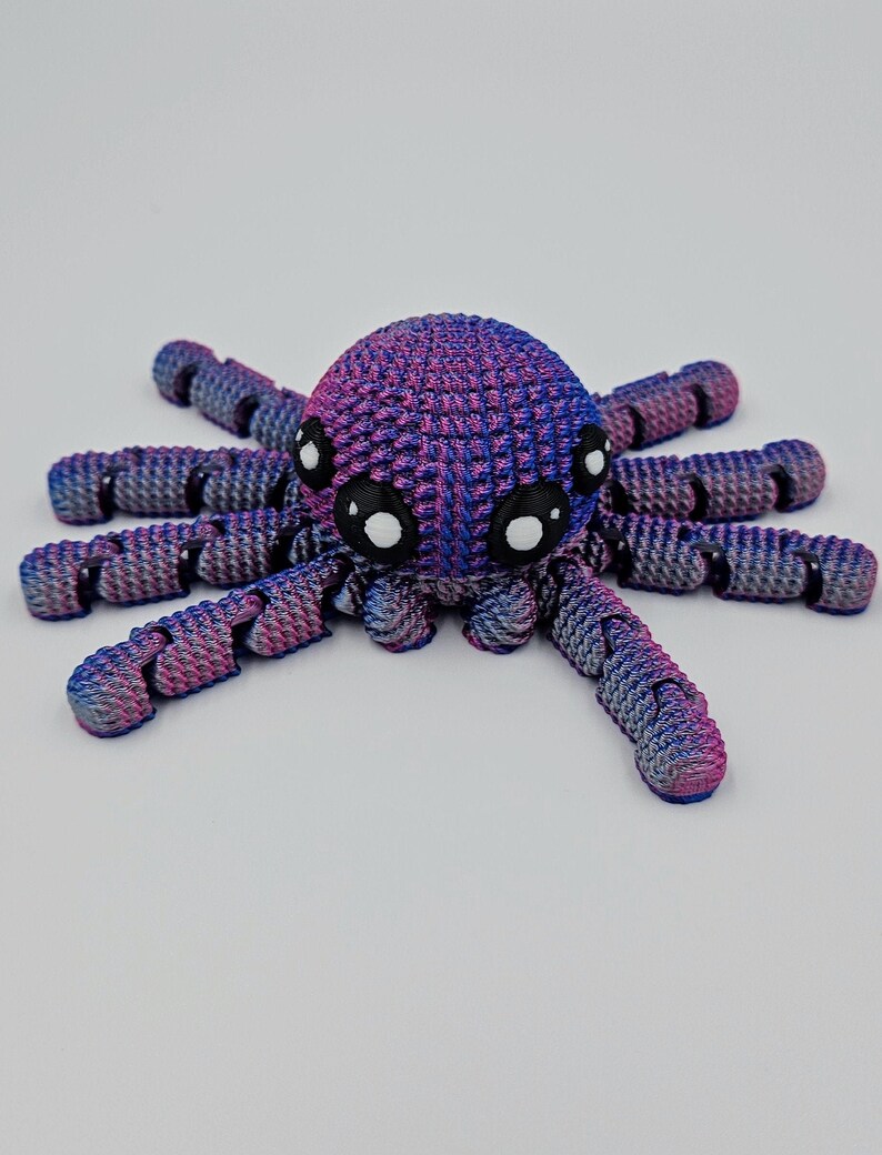 Op de afbeelding: Een kleine, 3D-geprinte octopus met een roze en blauwe kleurverloop. De octopus heeft acht tentakels en grote, zwarte ogen.