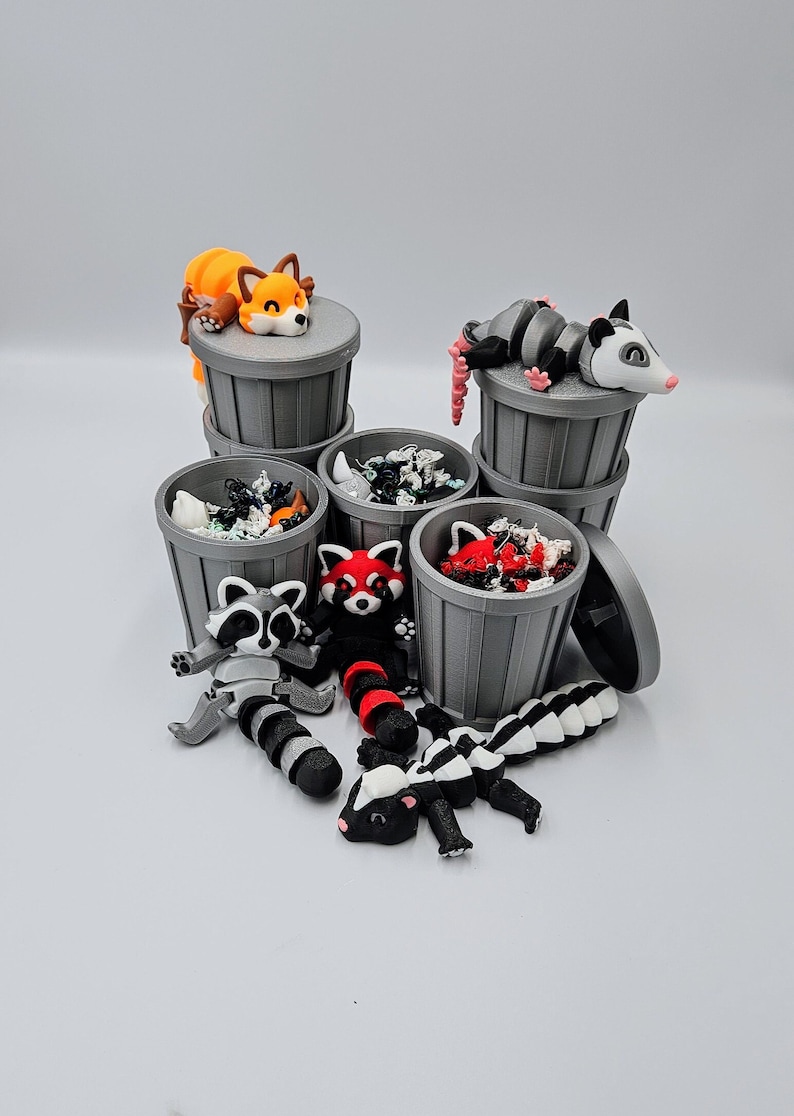 May include: A collection of miniature gray trash cans, each filled with colorful debris and topped with various animal figurines. The figurines include a fox, opossum, raccoon, red panda, and skunk. The animals are in various poses.