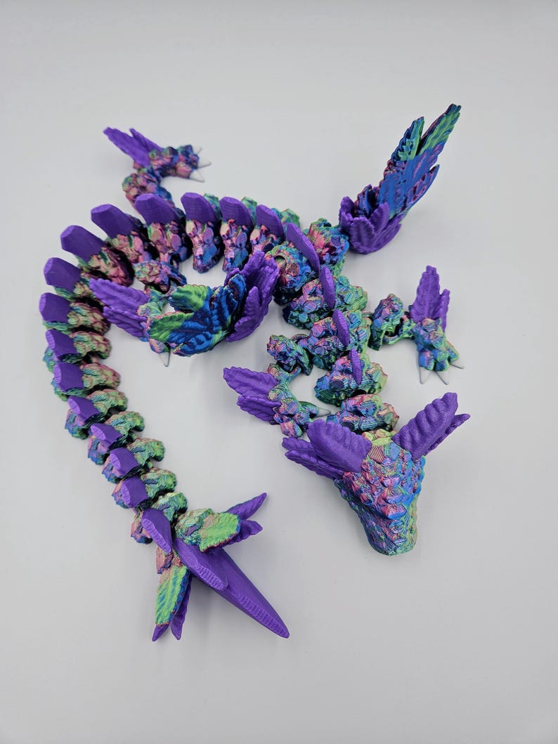 May include: A 3D printed dragon figurine with a purple, green, and blue iridescent finish. The dragon is posed in a curled position with its head raised and its wings spread out.