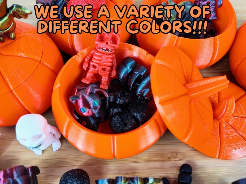 May include: A variety of small, colorful, 3D printed figurines are displayed inside orange pumpkin-shaped containers. The text "WE USE A VARIETY OF DIFFERENT COLORS!!!" is visible in the image.