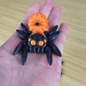Puede incluir: Una ara&ntilde;a impresa en 3D de color negro y naranja con ojos grandes. La ara&ntilde;a tiene un cuerpo con forma de calabaza.