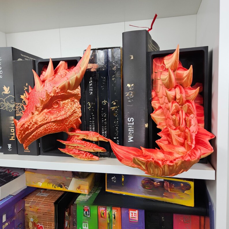 May include: A shelf arrangement featuring a red and gold dragon head, a dragon tail, and three small dragon wings. The dragon decor is placed among black books with gold lettering. The dragon head is on the left, the tail on the right.
