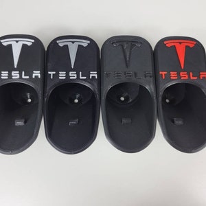 May include: Four black plastic Tesla car cup holders with the Tesla logo in white, silver, and red.