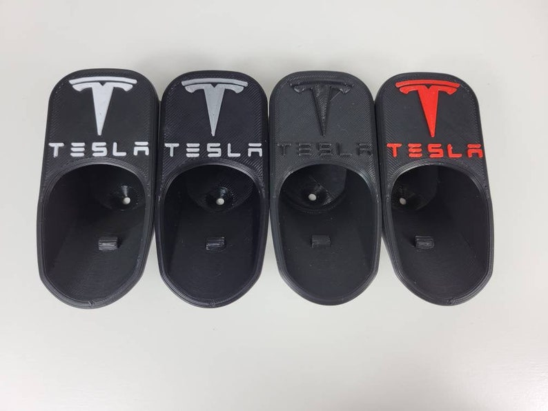 May include: Four black plastic Tesla car cup holders with the Tesla logo in white, silver, and red.