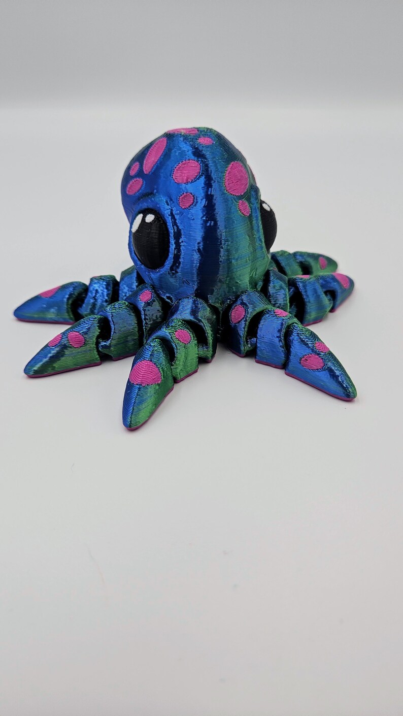 Puede incluir: Un pulpo impreso en 3D azul y verde con lunares rosas y grandes ojos negros.