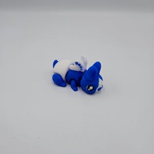 K&ouml;nnte beinhalten: Ein kleines blaues und wei&szlig;es Plastikspielzeugkaninchen mit einem wei&szlig;en Ohr und einem wei&szlig;en Fleck auf der Nase. Das Kaninchen liegt auf der Seite mit dem Kopf nach rechts gedreht.