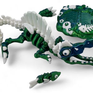 May include: A green and white skeleton of a sea monster with a blue and white head. The monster is holding a small green and white fish in its mouth. The monster is on a green and white rock with white flowers.