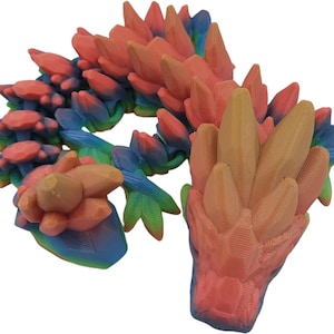K&ouml;nnte beinhalten: Eine 3D-gedruckte Drachenfigur mit einem Regenbogen-Farbverlauf. Der Drache ist zusammengerollt, mit erhobenem Kopf und ausgebreiteten Fl&uuml;geln. Der Drache ist aus glattem Kunststoff gefertigt.