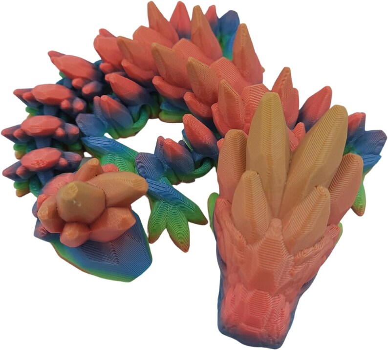 K&ouml;nnte beinhalten: Eine 3D-gedruckte Drachenfigur mit einem Regenbogen-Farbverlauf. Der Drache ist zusammengerollt, mit erhobenem Kopf und ausgebreiteten Fl&uuml;geln. Der Drache ist aus glattem Kunststoff gefertigt.