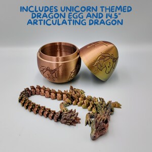 May include: A gold and green articulated dragon toy with a unicorn design. The dragon is made up of multiple connected pieces and comes with a matching dragon egg. The egg is a small, round container with a lid.