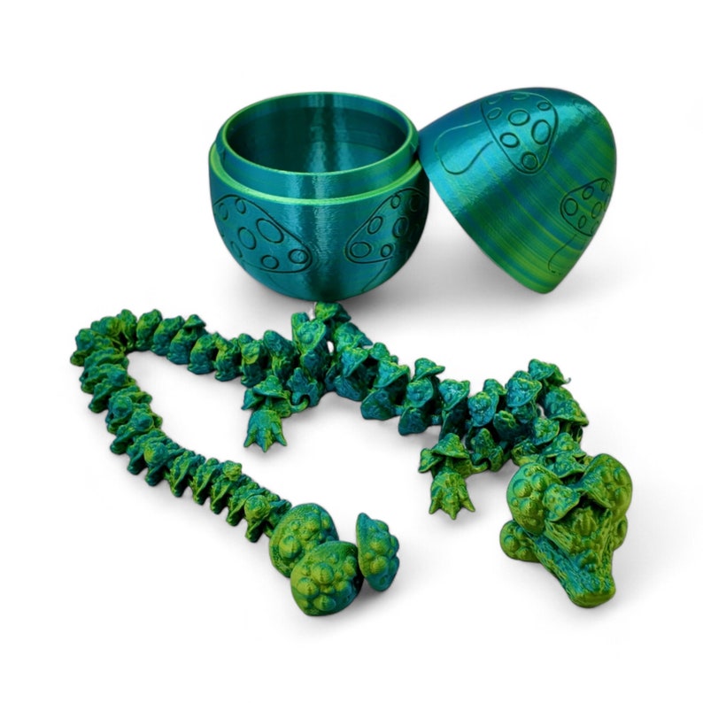 May include: A green and blue 3D printed alligator toy with a mushroom design. The alligator is made up of multiple pieces that can be connected together. The alligator is also a container with a lid shaped like a mushroom.