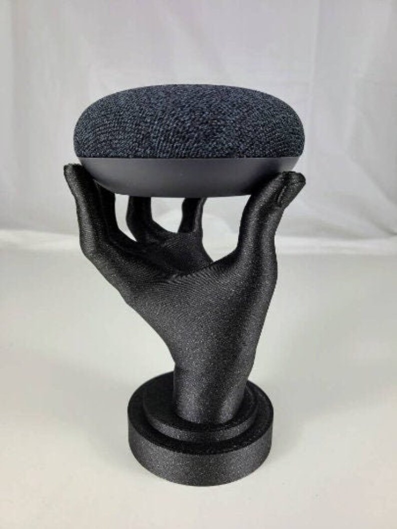 Op de afbeelding: Een zwarte Google Home slimme speaker staat op een zwarte handvormige standaard. De standaard heeft een ronde basis.