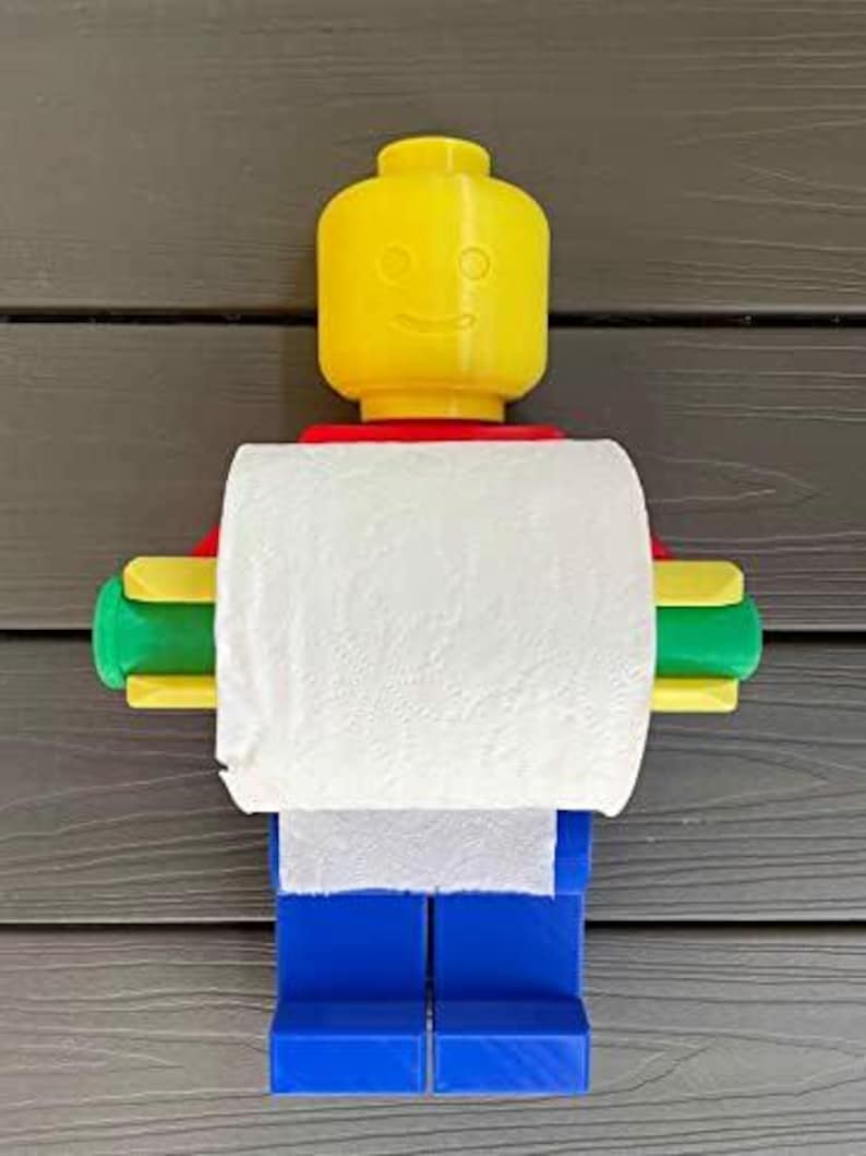 K&ouml;nnte beinhalten: Ein neuartiger Toilettenpapierhalter in Form eines gelben Lego-Figurenkopfes mit rotem Hals, gr&uuml;nen und gelben Armen und blauen Beinen. Der Halter ist f&uuml;r eine Rolle wei&szlig;es Toilettenpapier konzipiert.