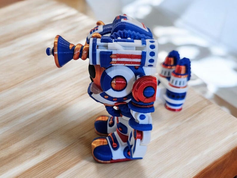 May include: A 3D printed robot toy in blue, white and red. The robot has a large head with a circular eye and a long, curved arm with a horn-like structure. The robot is standing on a wooden surface.