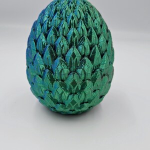May include: A green dragon egg with a textured, scaly surface. The egg is made of a 3D printed material and has a metallic sheen.