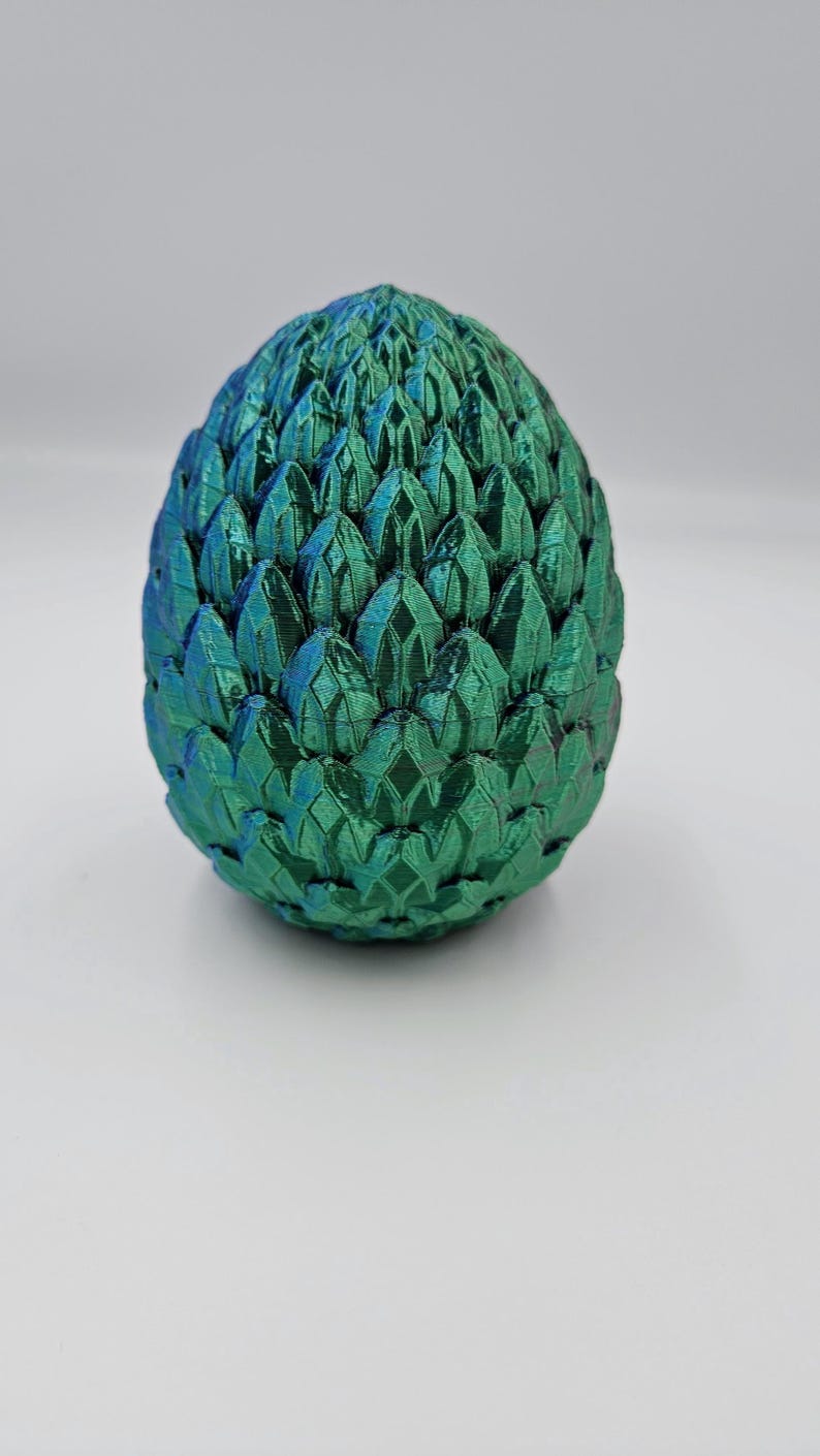 May include: A green dragon egg with a textured, scaly surface. The egg is made of a 3D printed material and has a metallic sheen.