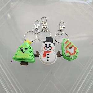 Pode incluir: Tr&ecirc;s chaveiros com tema natalino: uma &aacute;rvore de Natal verde que pisca, um boneco de neve branco com uma echarpe vermelha e um gnomo verde com um chap&eacute;u vermelho.