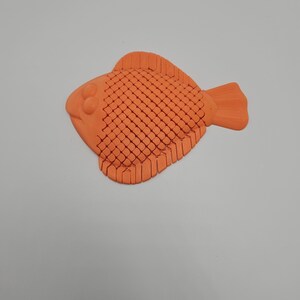 May include: An orange, stylized fish figurine with a textured body and fins. The fish has a rounded shape with a detailed scale pattern and is likely made of plastic or a similar material. The figurine is a decorative item.