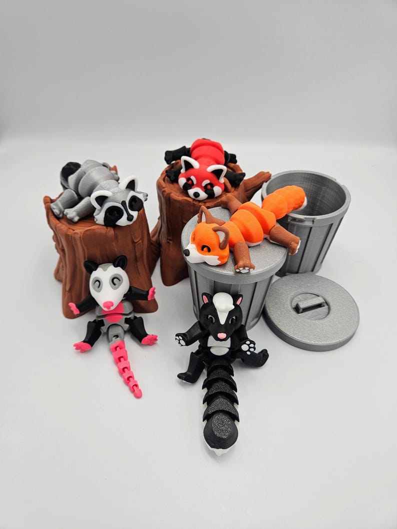May include: A set of five small animal figurines, including a raccoon, red panda, fox, opossum, and skunk. The figurines are made of a gray plastic and are posed in various positions. The raccoon and red panda are lying on a brown tree stump, while the fox is lying in a gray trash can. The opossum and skunk are standing on the ground.