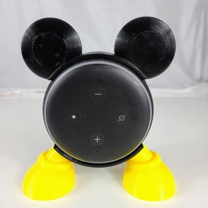 Puede incluir: Un altavoz Amazon Echo Dot negro con un dise&ntilde;o de Mickey Mouse impreso en 3D. El altavoz tiene pies amarillos y orejas negras.