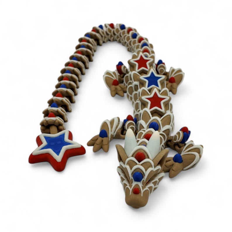May include: A whimsical, gingerbread dragon sculpture with a brown base, decorated with white icing and red and blue star accents. The dragon's body is segmented, with a curved tail and detailed head, perfect for holiday decor.