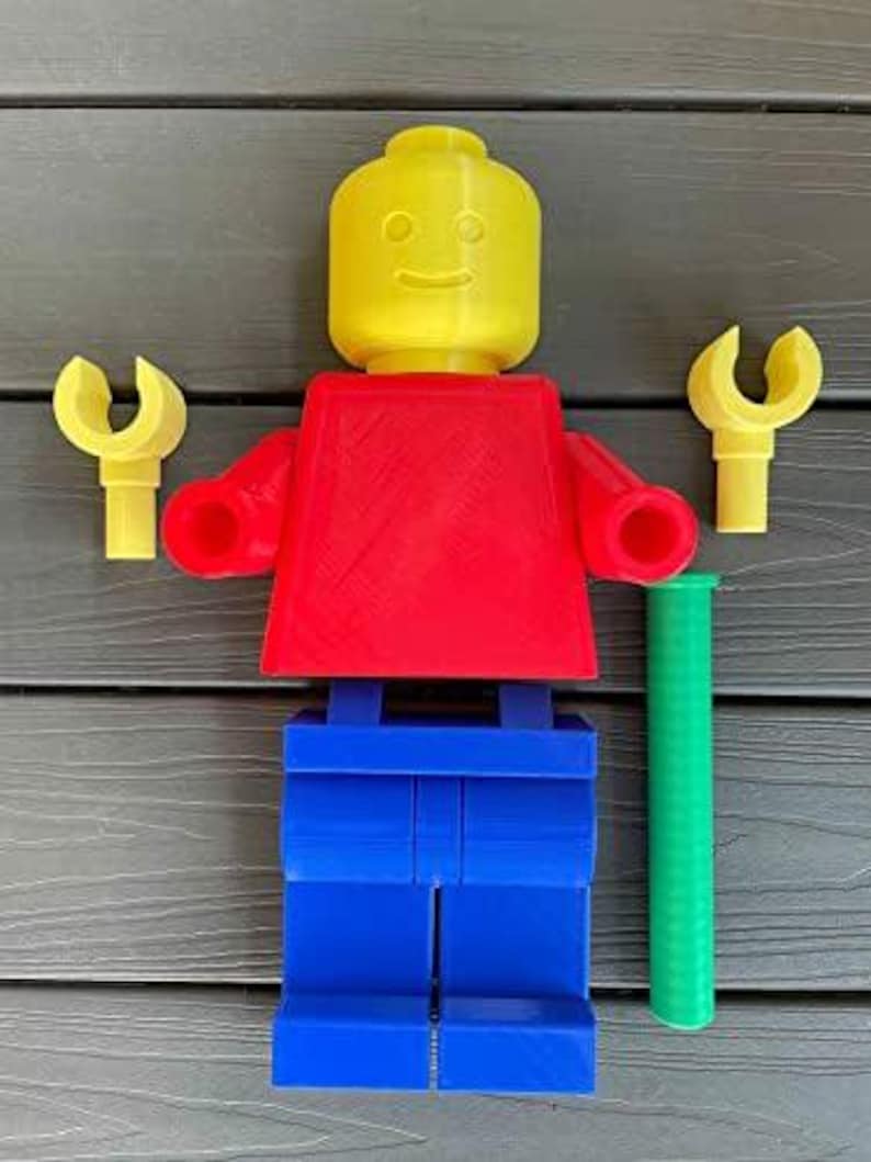 K&ouml;nnte beinhalten: Eine gro&szlig;e Lego-Figur in den Grundfarben: gelber Kopf, roter Torso und blaue Beine. Sie hat gelbe H&auml;nde und einen gr&uuml;nen Zylinder. Die Figur ist aus Kunststoff und als Spielzeug konzipiert.