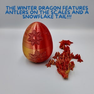 K&ouml;nnte beinhalten: Ein rotes und goldenes Ei mit Schneeflockenmustern und eine rote und goldene Drachenfigur mit Schneeflockenschuppen. Der Text "THE WINTER DRAGON FEATURES ANTLERS ON THE SCALES AND A SNOWFLAKE TAIL!!!" befindet sich &uuml;ber dem Ei.