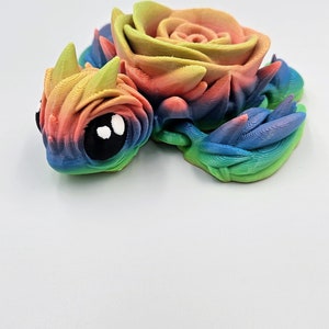 May include: A 3D printed rainbow colored figurine of a dragon with a rose on its back.