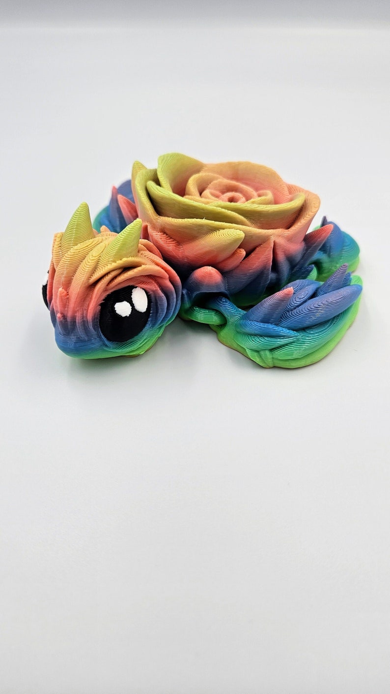 May include: A 3D printed rainbow colored figurine of a dragon with a rose on its back.