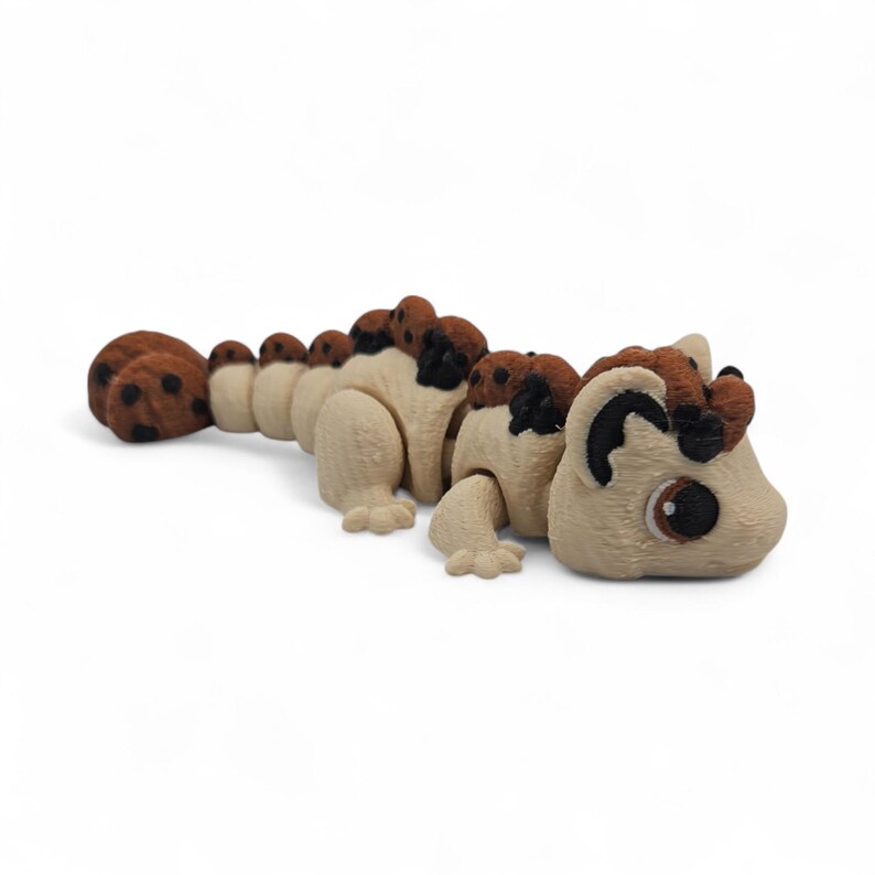 May include: A beige and brown articulated toy, resembling a lizard or dragon. The toy has a series of segments, with brown spots and a head crest. The eyes are dark brown.