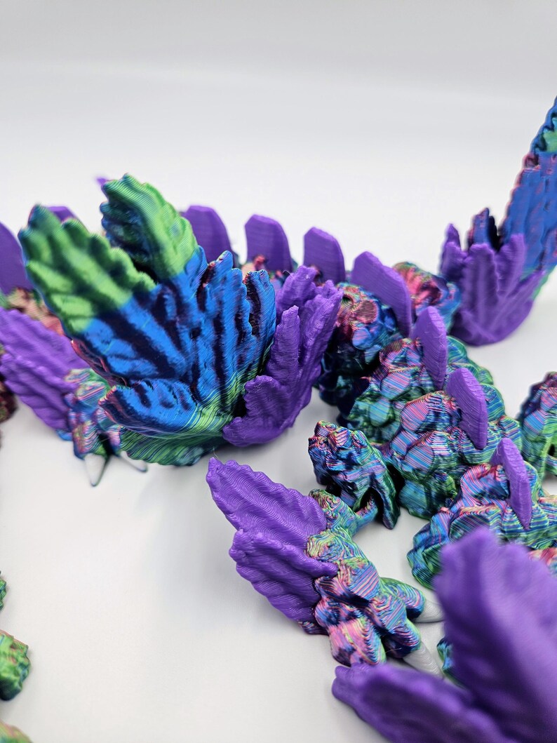 May include: A close-up of a 3D printed dragon's scales, featuring a vibrant iridescent finish with shades of purple, blue, green, and pink.