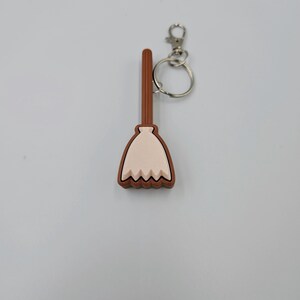 May include: A brown and white plastic broom keychain with a silver key ring.