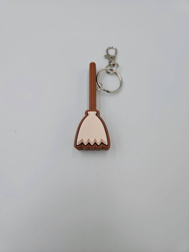 May include: A brown and white plastic broom keychain with a silver key ring.