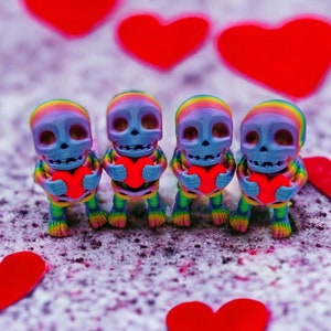 May include: Five small rainbow skeleton figurines holding red hearts. The skeletons are standing on a white surface with red hearts scattered around them.