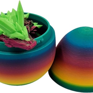 May include: A rainbow-coloured plastic egg opens to reveal a green and purple crystal dragon figurine inside.