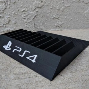 May include: A black plastic stand with slots for storing video game discs. The stand has the PlayStation 4 logo printed on the front.