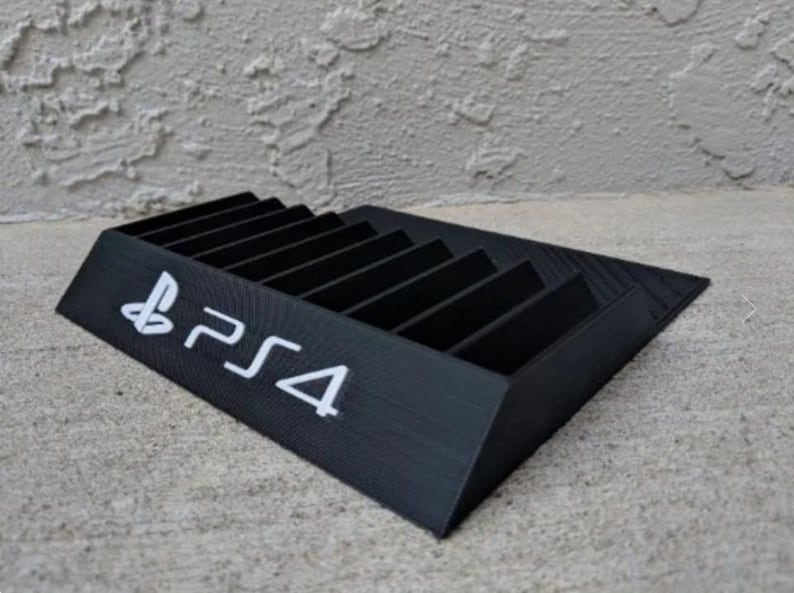 May include: A black plastic stand with slots for storing video game discs. The stand has the PlayStation 4 logo printed on the front.