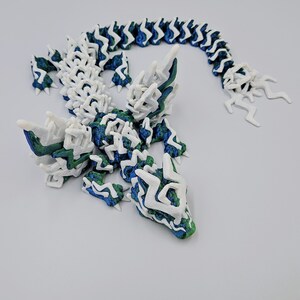 May include: A 3D printed lizard sculpture with a white, blue and green colour scheme. The lizard is posed in a standing position with its tail curled up behind it.