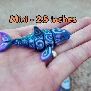 May include: A small, blue and green patterned shark figurine, approximately 2.5 inches long. The figurine is made of plastic and has a detailed design. "Mini - 2.5 inches" is written in orange text on the image.