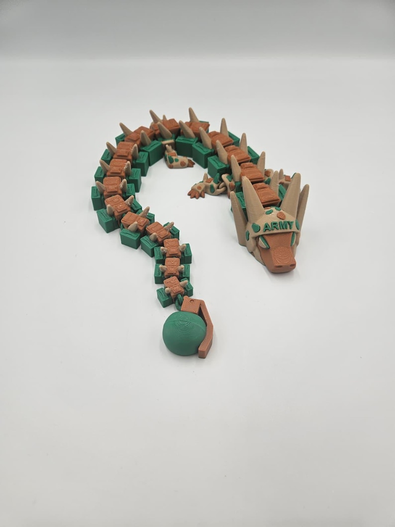 Pode incluir: Um brinquedo de drag&atilde;o articulado impresso em 3D em tons de castanho, verde e bege. O drag&atilde;o tem um corpo segmentado, uma cabe&ccedil;a com a palavra "ARMY" impressa e uma granada verde na ponta da cauda. O brinquedo &eacute; projetado para ser flex&iacute;vel e pos&aacute;vel.