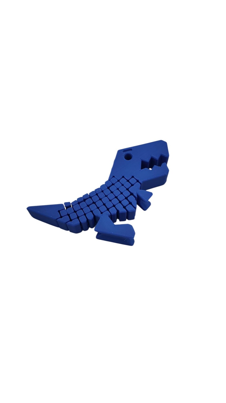 Puede incluir: Un juguete de dinosaurio azul articulado. El juguete est&aacute; hecho de peque&ntilde;os bloques cuadrados que forman el cuerpo, la cabeza y la cola. El dinosaurio tiene una boca con dientes y patas peque&ntilde;as. El juguete est&aacute; sobre un fondo blanco.