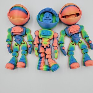 May include: Three colourful astronaut figurines with rainbow gradient paint. Each figurine has a removable helmet and a detailed body with articulated joints.