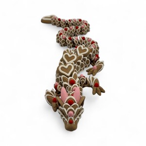 May include: A whimsical, brown gingerbread dragon with white icing details and heart-shaped accents. The dragon features pink ears and red dot embellishments, creating a festive and decorative design. This unique item is perfect for holiday decor.