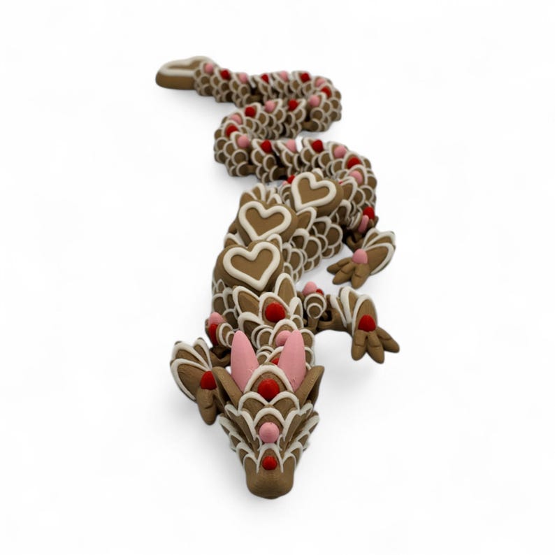 May include: A whimsical, brown gingerbread dragon with white icing details and heart-shaped accents. The dragon features pink ears and red dot embellishments, creating a festive and decorative design. This unique item is perfect for holiday decor.