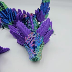 May include: A 3D printed dragon figurine with iridescent purple and green scales. The dragon's head is facing forward with its mouth closed. The dragon's wings are spread out behind it.