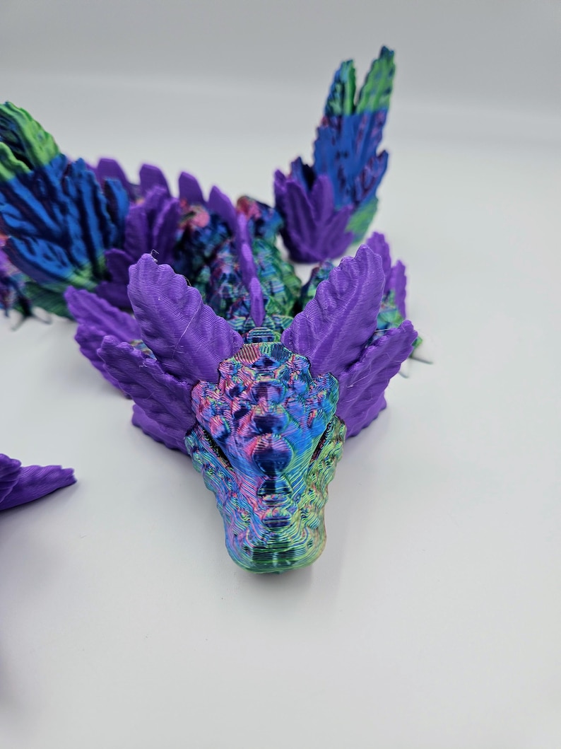 May include: A 3D printed dragon figurine with iridescent purple and green scales. The dragon's head is facing forward with its mouth closed. The dragon's wings are spread out behind it.
