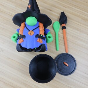 Puede incluir: Una figura caprichosa con tem&aacute;tica de Halloween de una bruja con sombrero negro y vestido azul. La bruja tiene trenzas naranjas, manos verdes y adornos en forma de murci&eacute;lago. Incluye un caldero, cuchara y escoba.